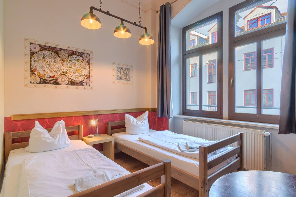 A room with two beds, a table, and a window with a view of buildings.