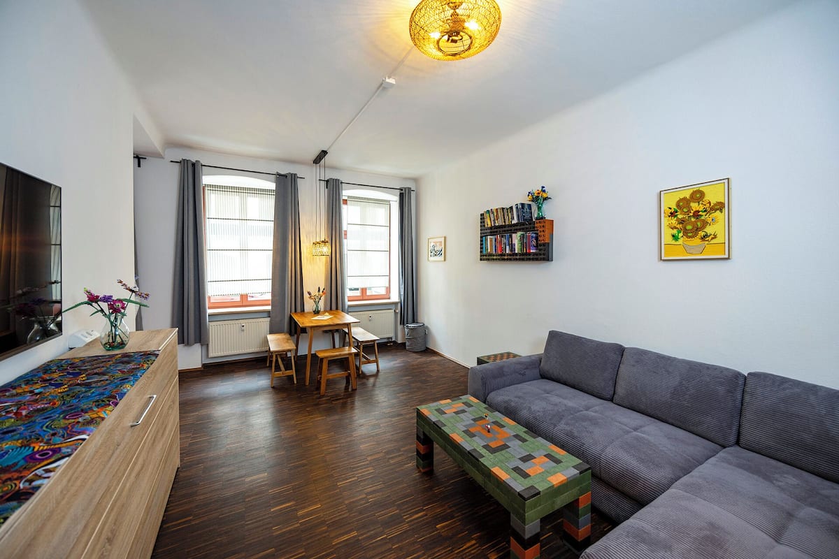A modern living room with a sofa, a coffee table, a dining table with chairs, a bookshelf, and a window with curtains.