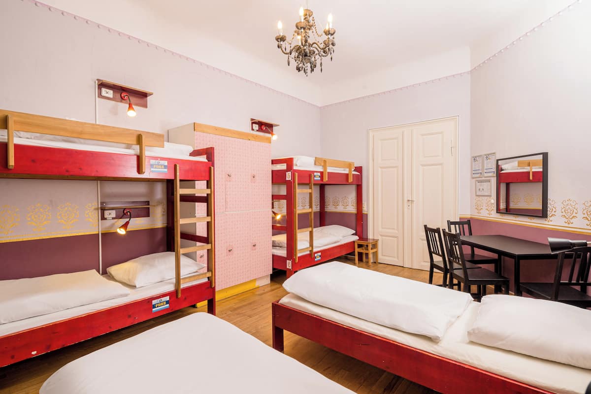 A dormitory room with bunk beds, a desk, chairs, and a chandelier.