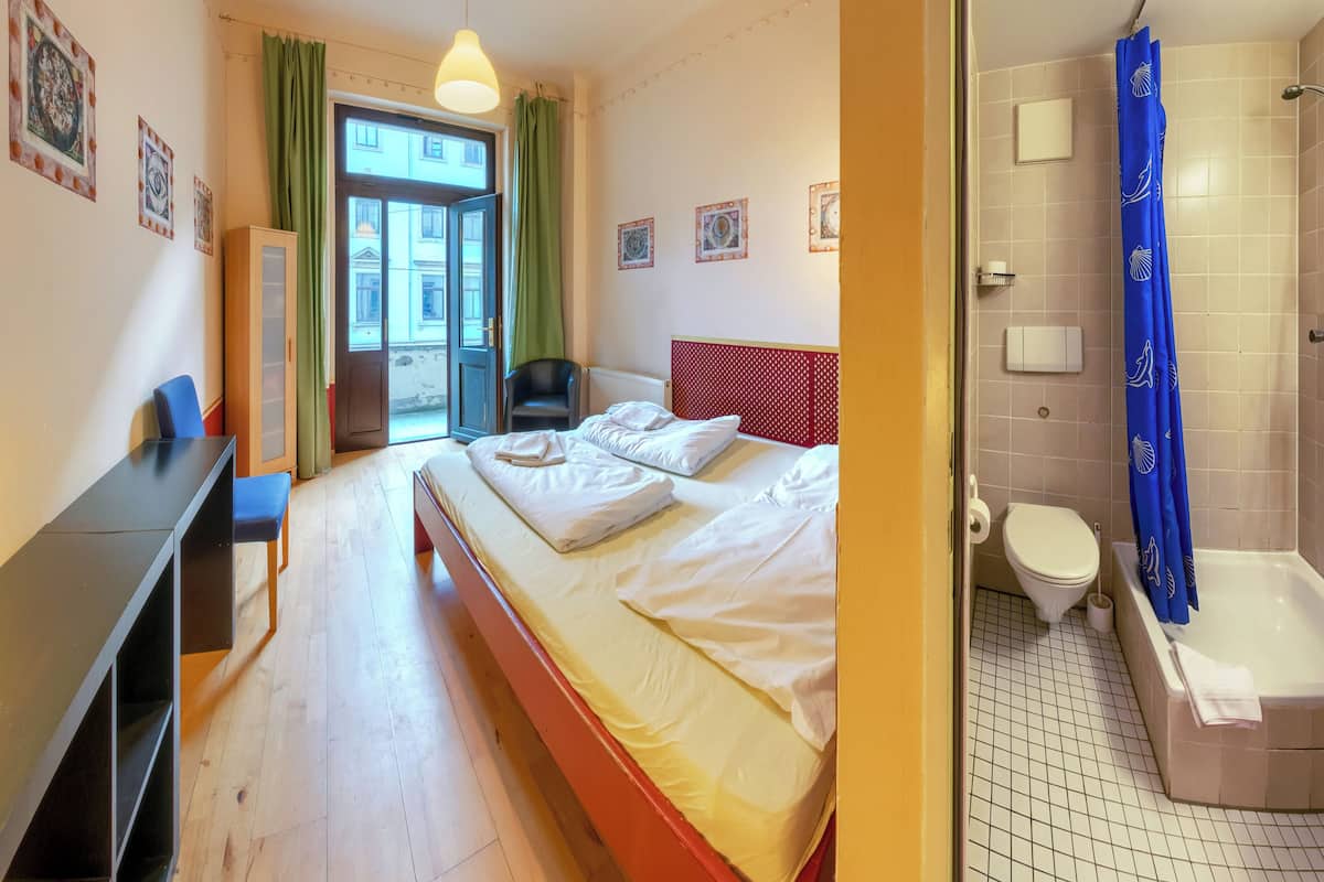 A hotel room with a bed, a desk, a chair, a window with curtains, and a bathroom with a bathtub and toilet.