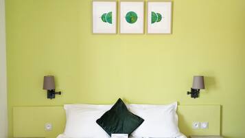 Habitación de hotel con una cama, dos mesitas de noche, un velador, una pared verde y tres cuadros enmarcados.