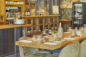 Un restaurante con una larga mesa de madera preparada para comer, copas de vino, botellas y una variedad de platos.