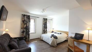 A bedroom with a bed, a desk with a laptop, a chair, a couch, and curtains.
