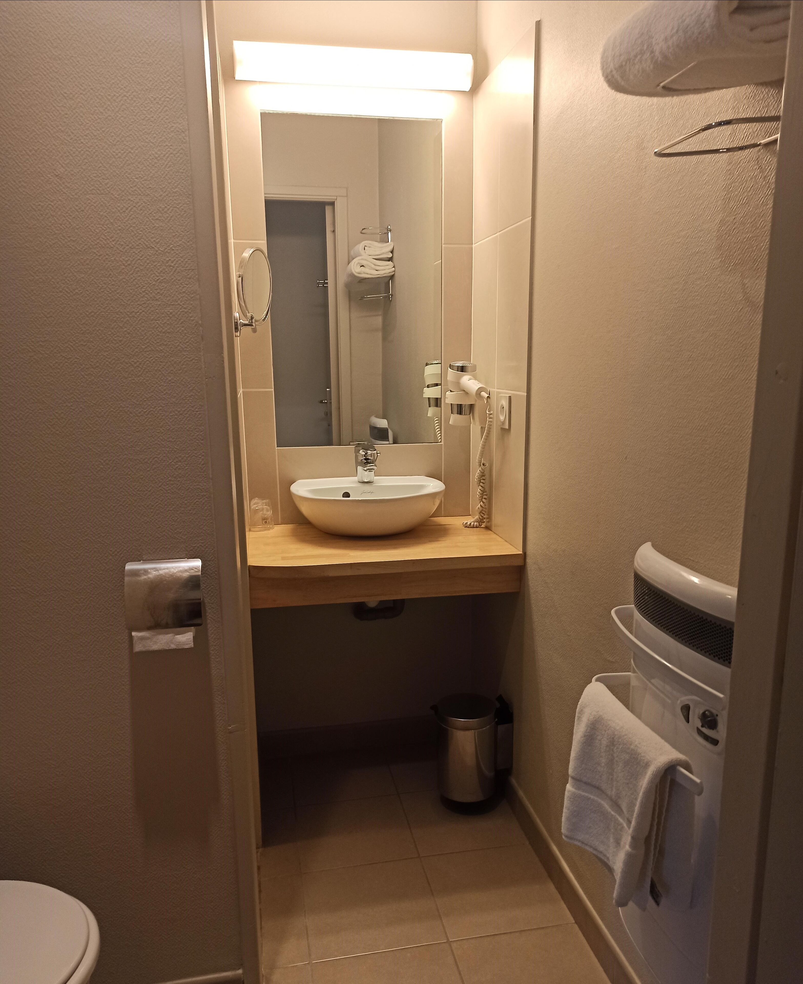 Une salle de bain équipée d’un lavabo, d’un miroir, d’un porte-serviettes et d’une poubelle.