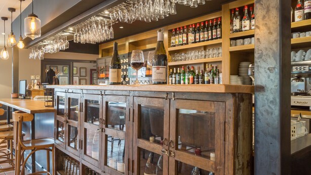 A bar area with wooden cabinets, wine bottles, and hanging glasses. - Le Nouvel (Portes-les-Valence)