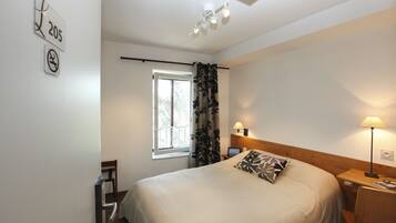 A bedroom with a bed, a window, a nightstand, a lamp, and a wall with a number sign.