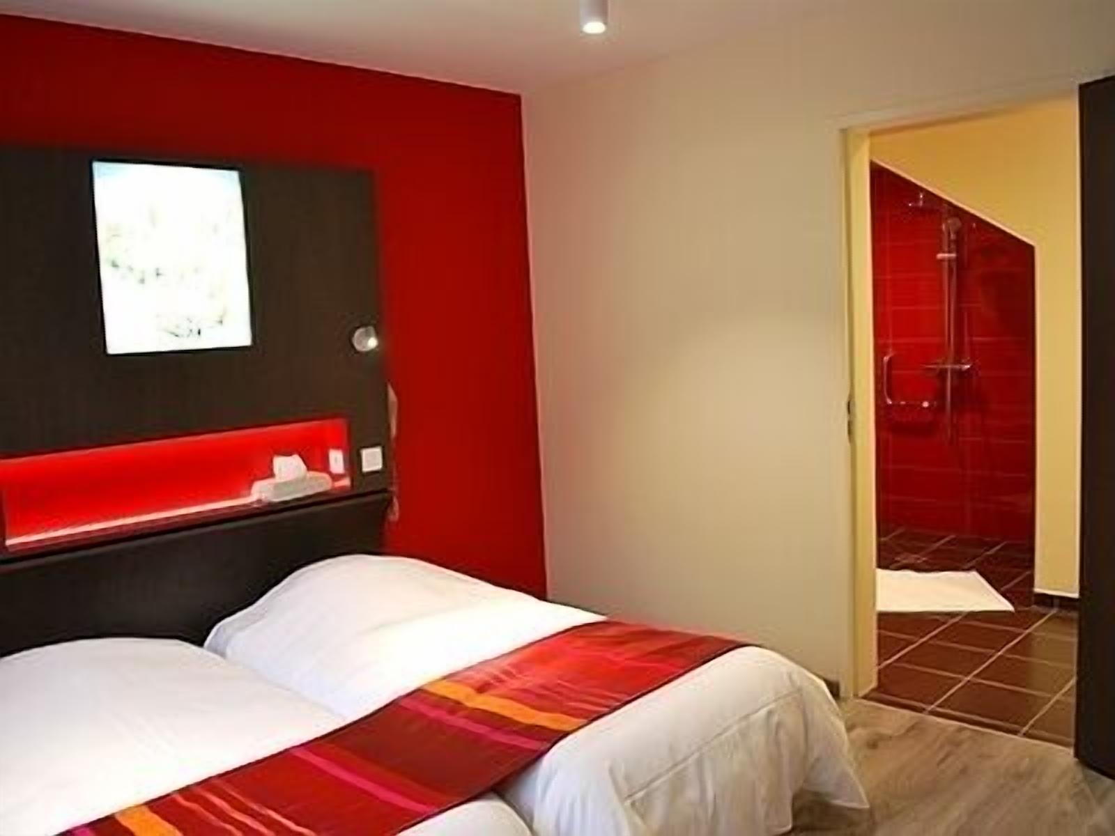 Habitación de hotel con cama, pared de acento roja y zona de ducha.