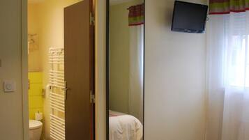Habitación de hotel con cama, mesita de noche, espejo, televisión y baño visible a través de una puerta abierta.