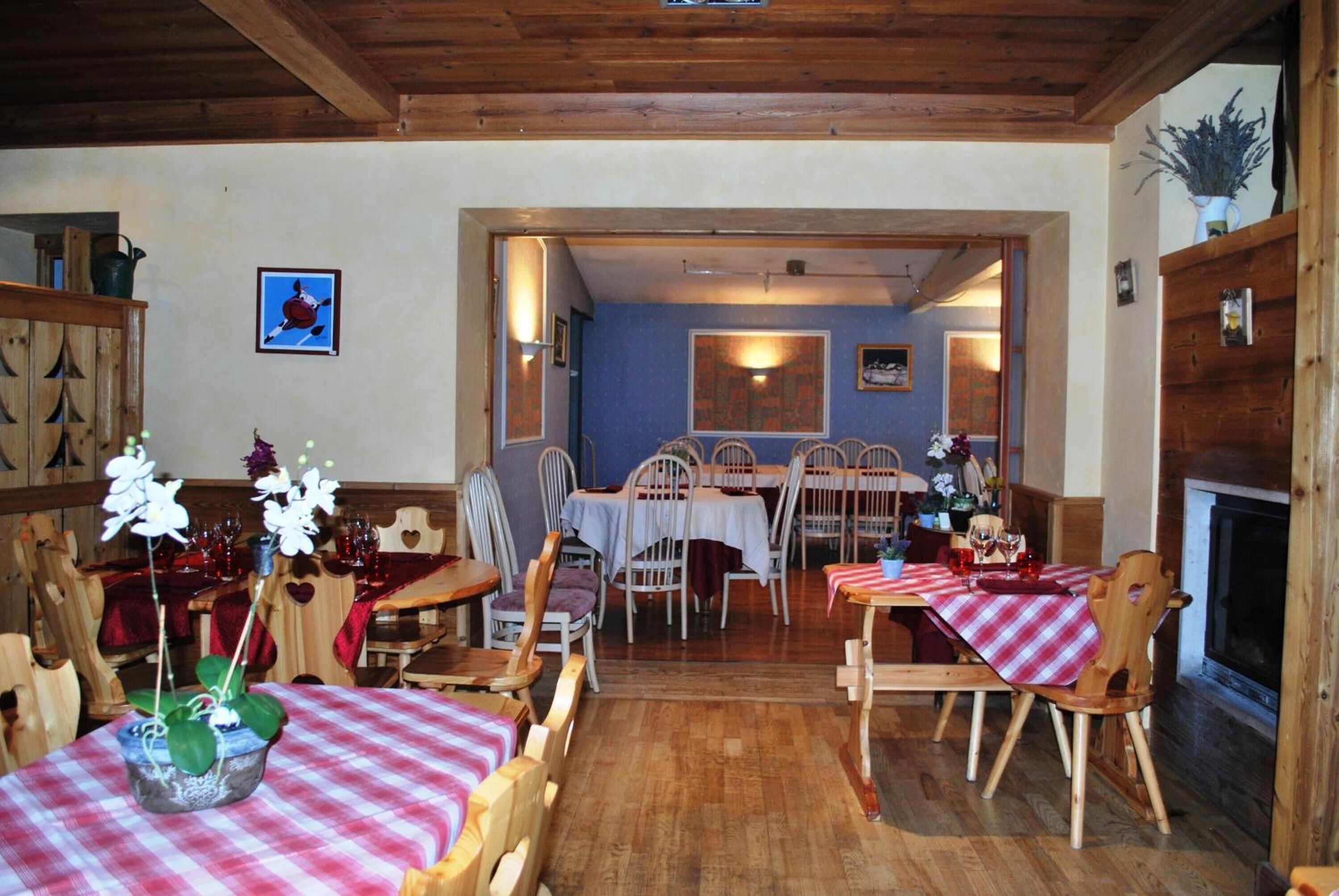 Un espace repas avec des tables et des chaises en bois, une cheminée et un mur bleu orné de tableaux encadrés.