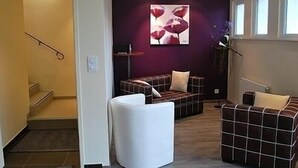 A modern living room with a sofa, a white armchair, and a coffee table. There is a staircase leading to another room. - Hôtel Restaurant Au Perce Neige (Bonnetage)