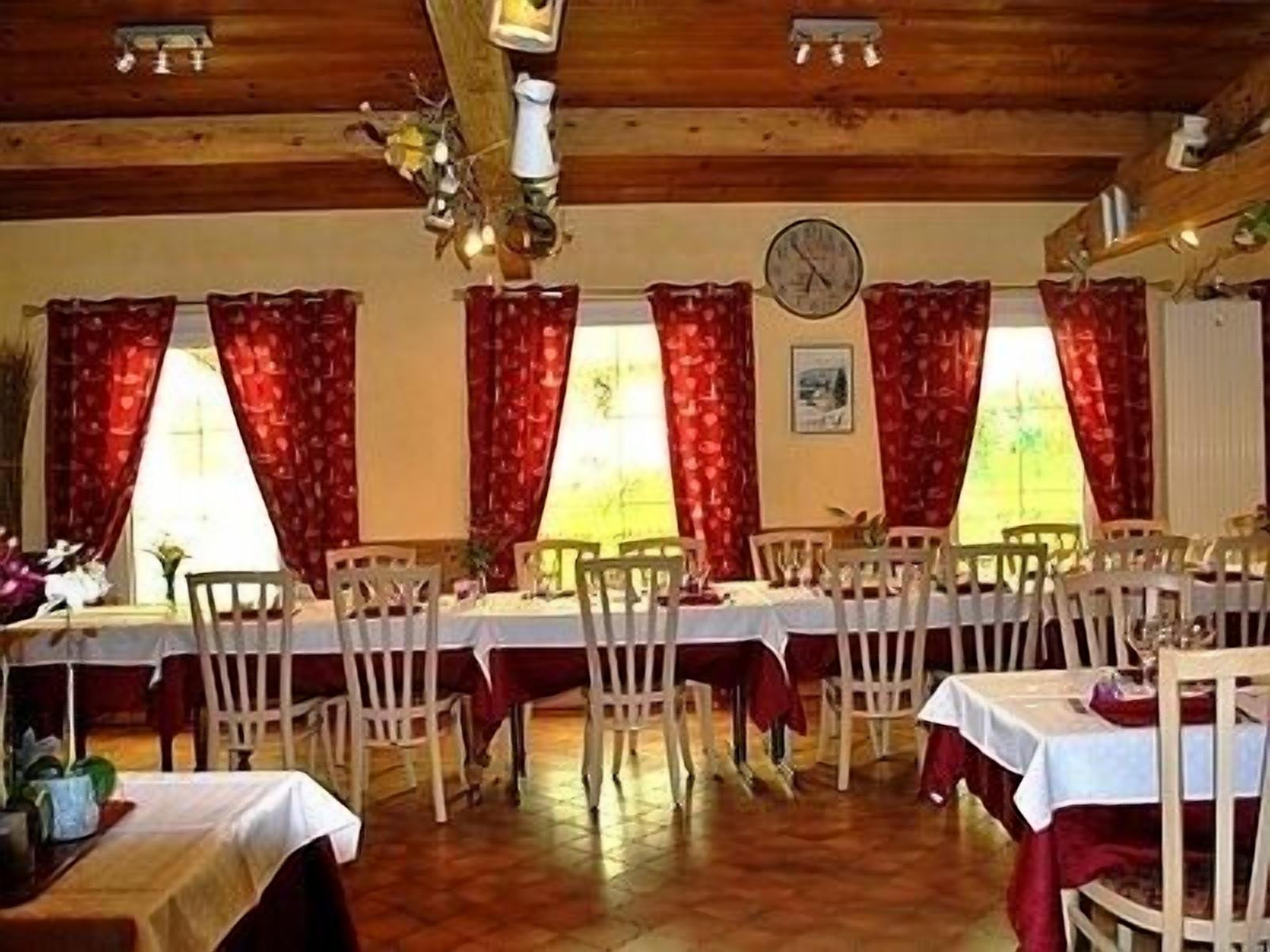 Zona pranzo con diversi tavoli e sedie, travi in legno al soffitto e tende rosse.