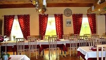 Zona pranzo con diversi tavoli e sedie, travi in legno al soffitto e tende rosse.