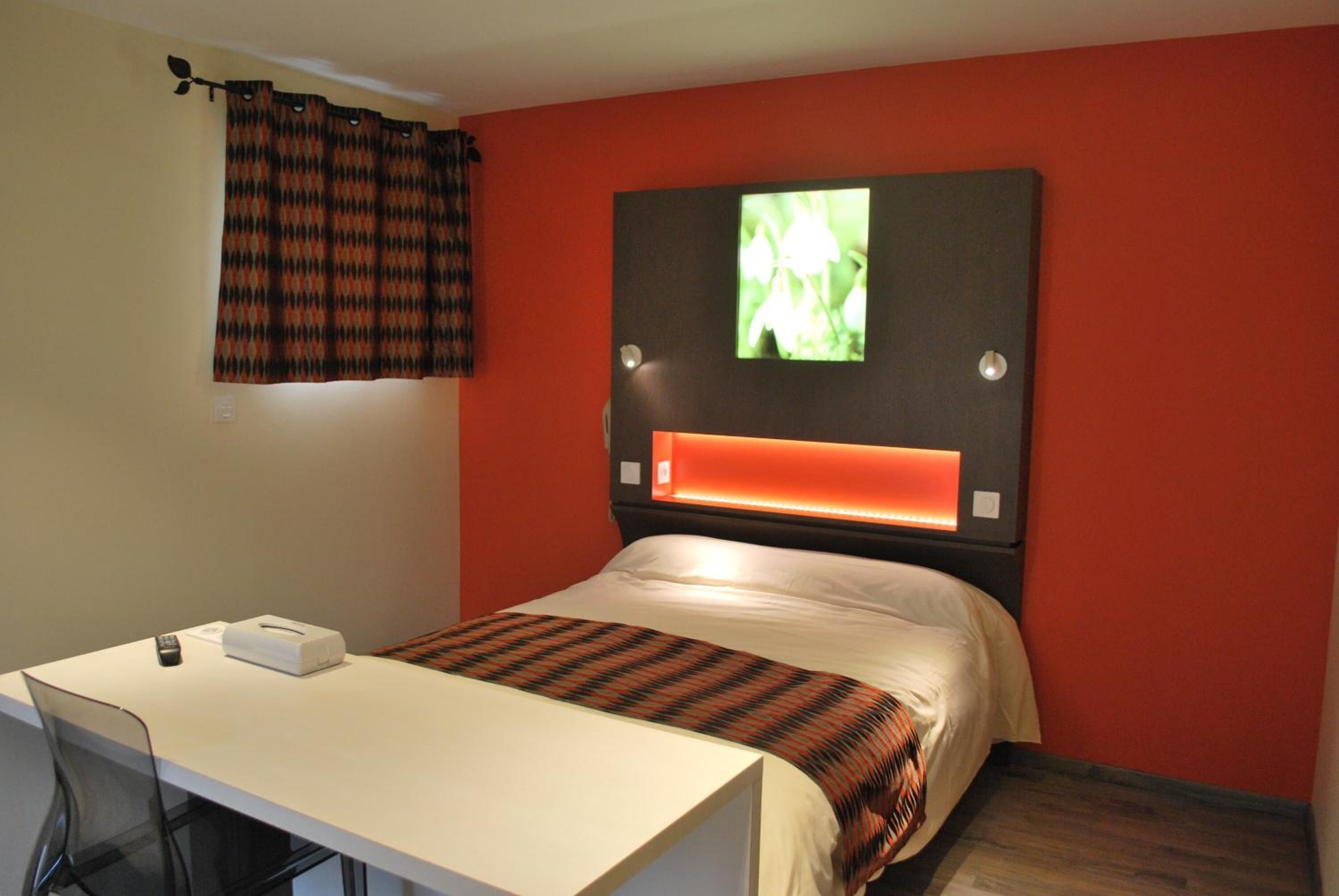Habitación de hotel con cama, escritorio, silla, televisor montado en la pared y cortina.