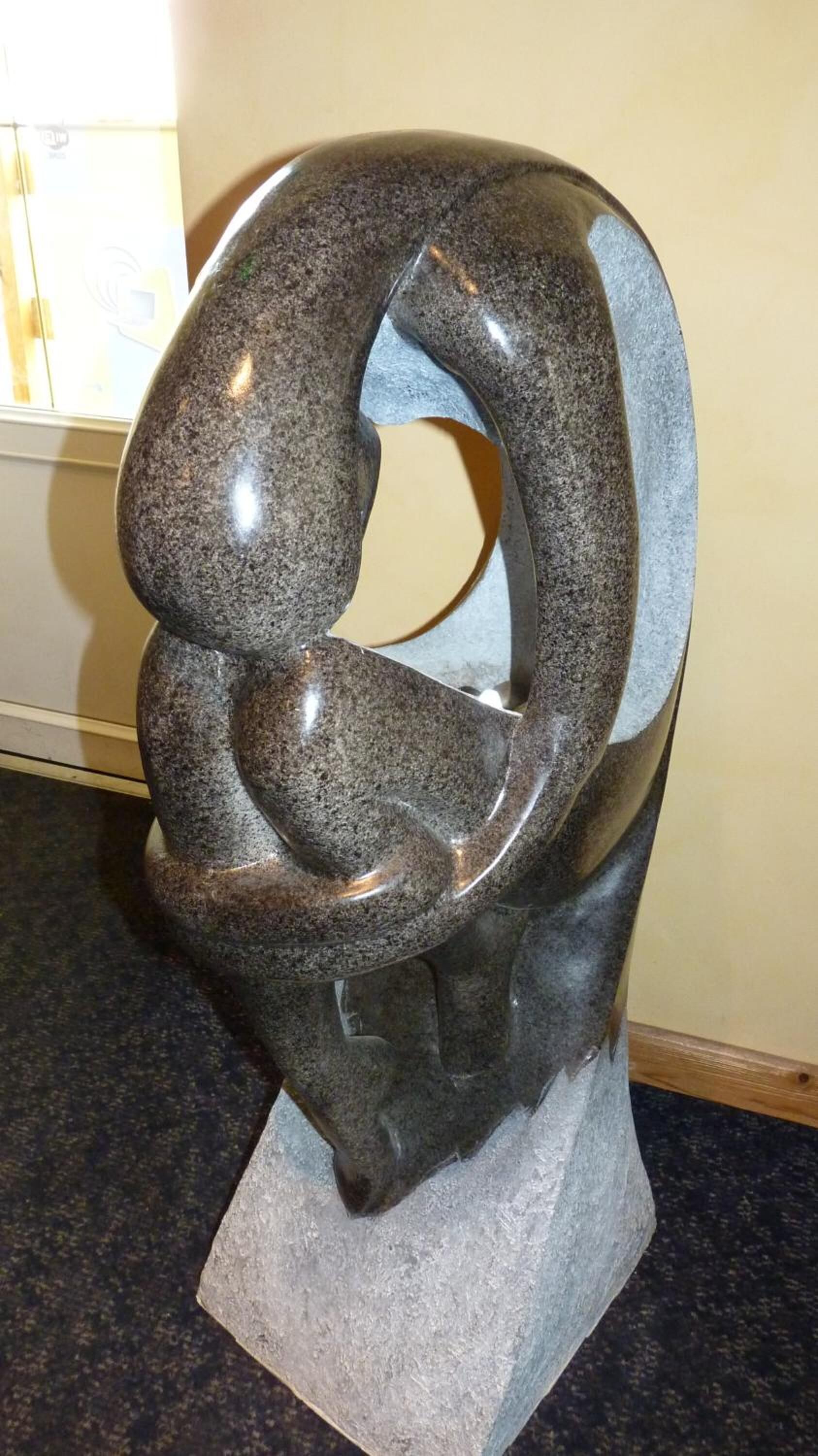 Una escultura de figura humana en una pose dinámica, hecha de piedra oscura, sobre un pedestal.