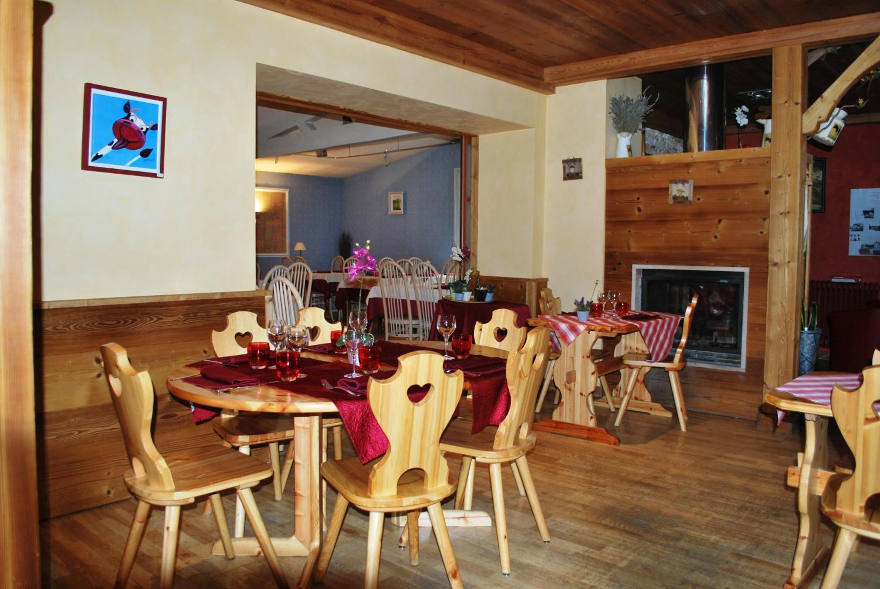 Ein Essbereich mit Holztischen und stuhlförmigen Herzchen, ein Kamin und eine blaue Wand mit einem gerahmten Bild.