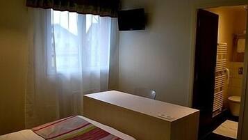 A hotel room with a bed, a desk, a chair, a TV on the wall, and a bathroom visible through an open door.