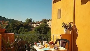 A balcony with a table set for breakfast, overlooking a hillside with houses. - Le Pont d'Or (Barjols)