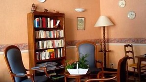 A room with a wooden bookshelf filled with books, a table with a plant, and two chairs. - Le Pont d'Or (Barjols)