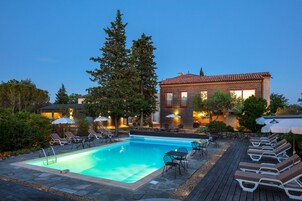Uma piscina com espreguiçadeiras e guarda-sóis, rodeada por um deck de madeira e um edifício com telhado de azulejos.