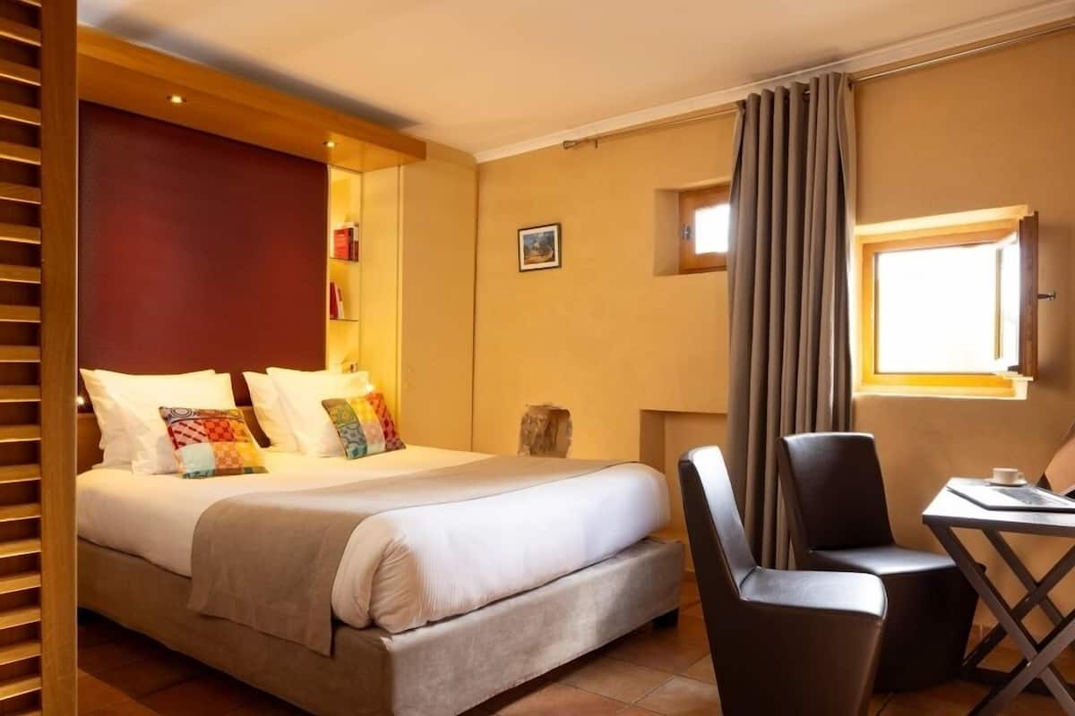 A hotel room with a bed, a desk, a chair, and a window with curtains.