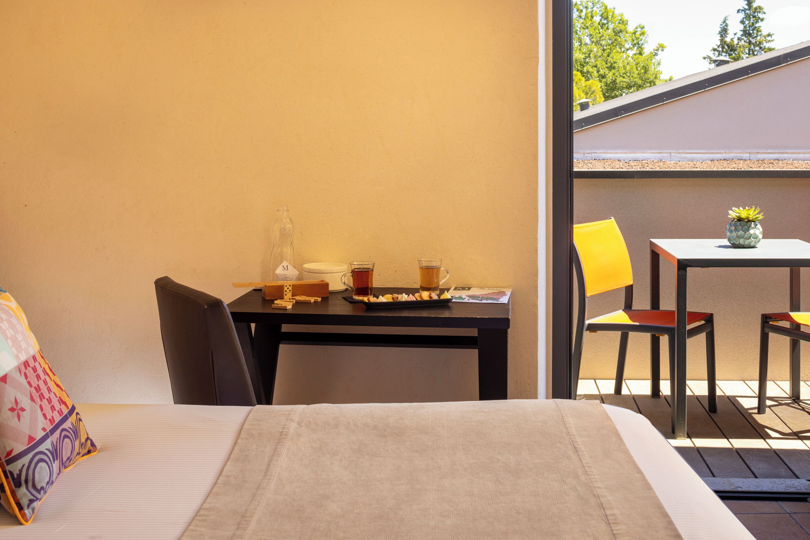 A room with a bed, a table with a vase and a cup, and a chair.