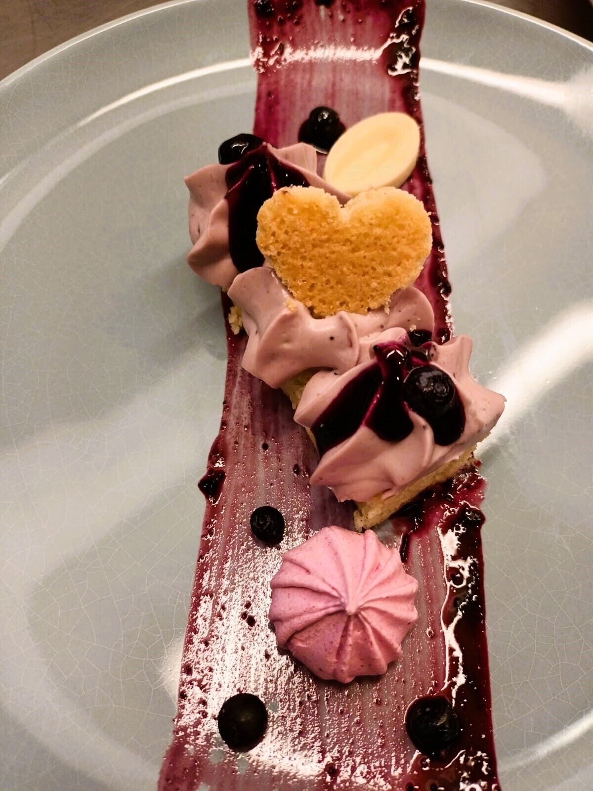 Un dessert composé d’un biscuit en forme de cœur et de motifs tourbillonnants roses, le tout présenté sur une assiette.
