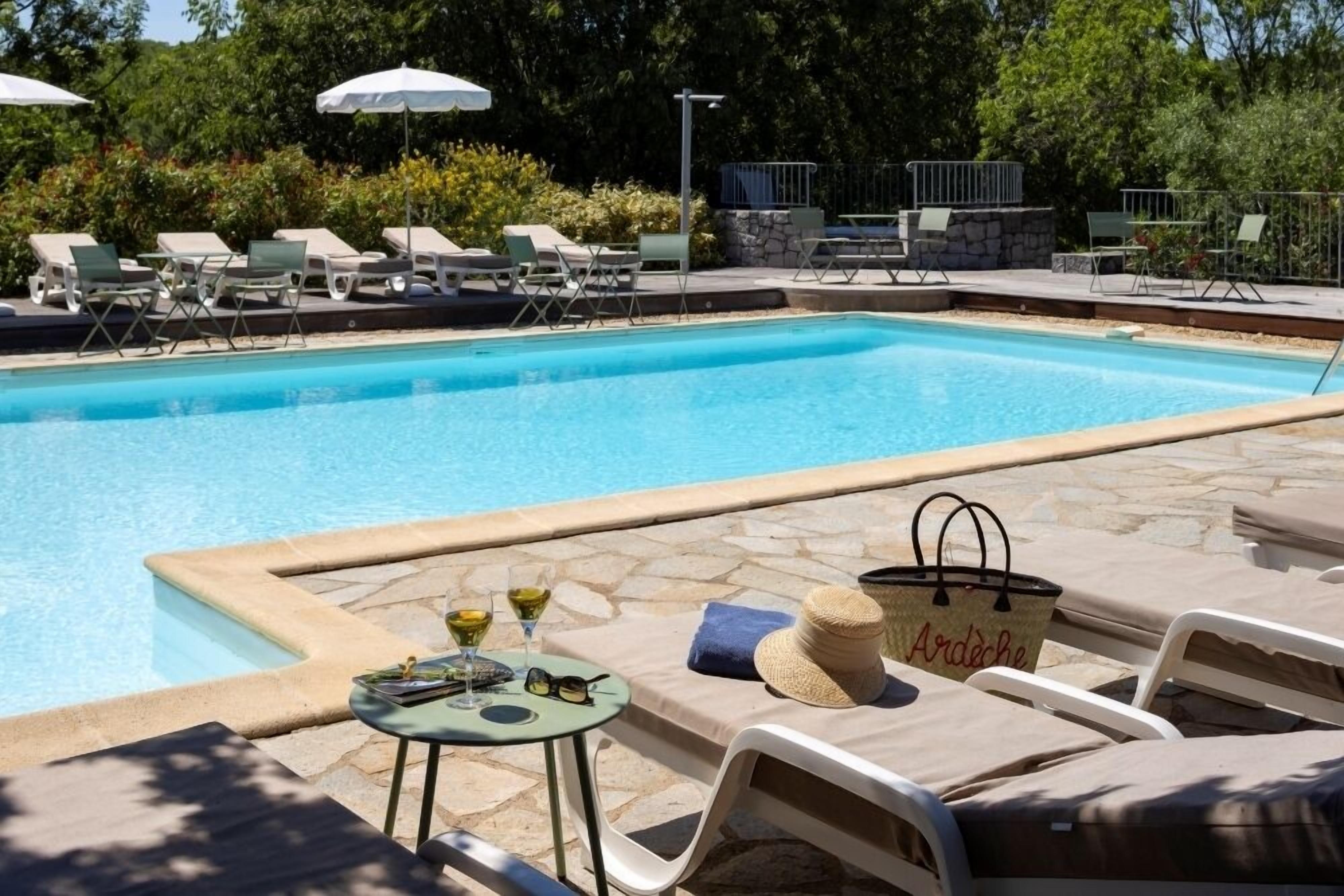 A swimming pool with lounge chairs and umbrellas, surrounded by stone tiles and greenery.
