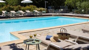 A swimming pool with lounge chairs and umbrellas, surrounded by stone tiles and greenery.