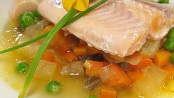Un plato con pescado, guisantes, zanahorias y una flor amarilla como decoración.