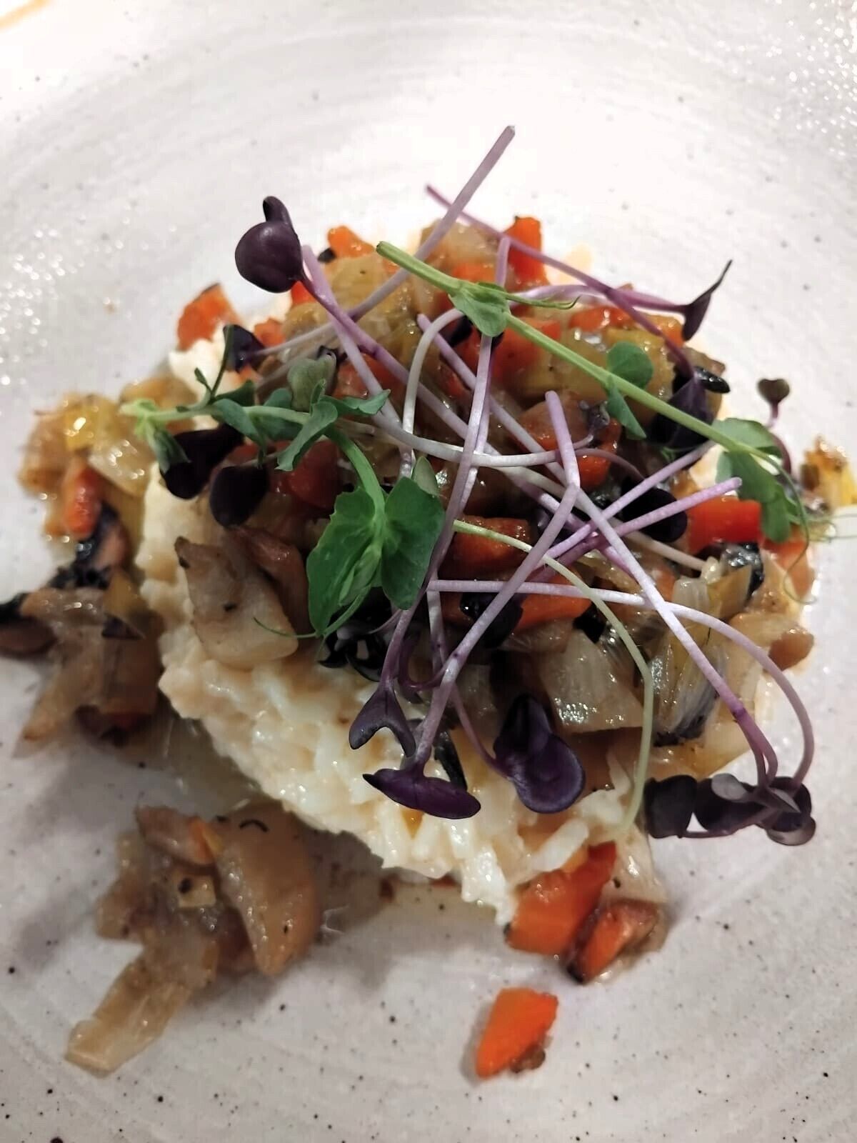 A dish with a creamy base, topped with vegetables and sprouts.