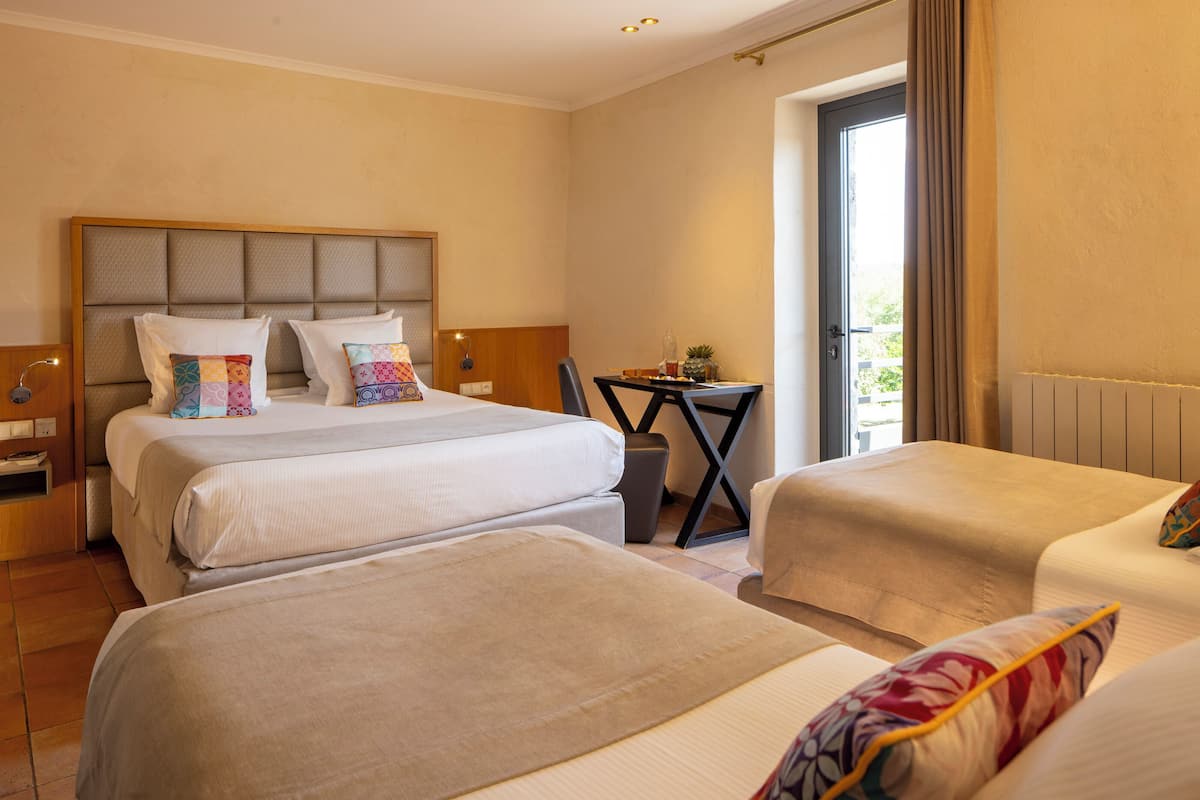 A hotel room with two beds, a small table with a plant, and a view of the outdoors.