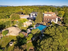 Una casa grande con piscina, rodeada de árboles y colinas.