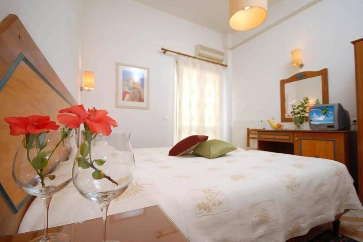 A hotel room with a bed, a desk with a computer, a mirror, and a window with curtains.