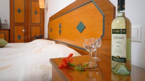 A hotel room with a wooden headboard, a bottle of Zdravitsa wine, and a glass on a bedside table. - Barbouni Hotel & Studios (Naxos)