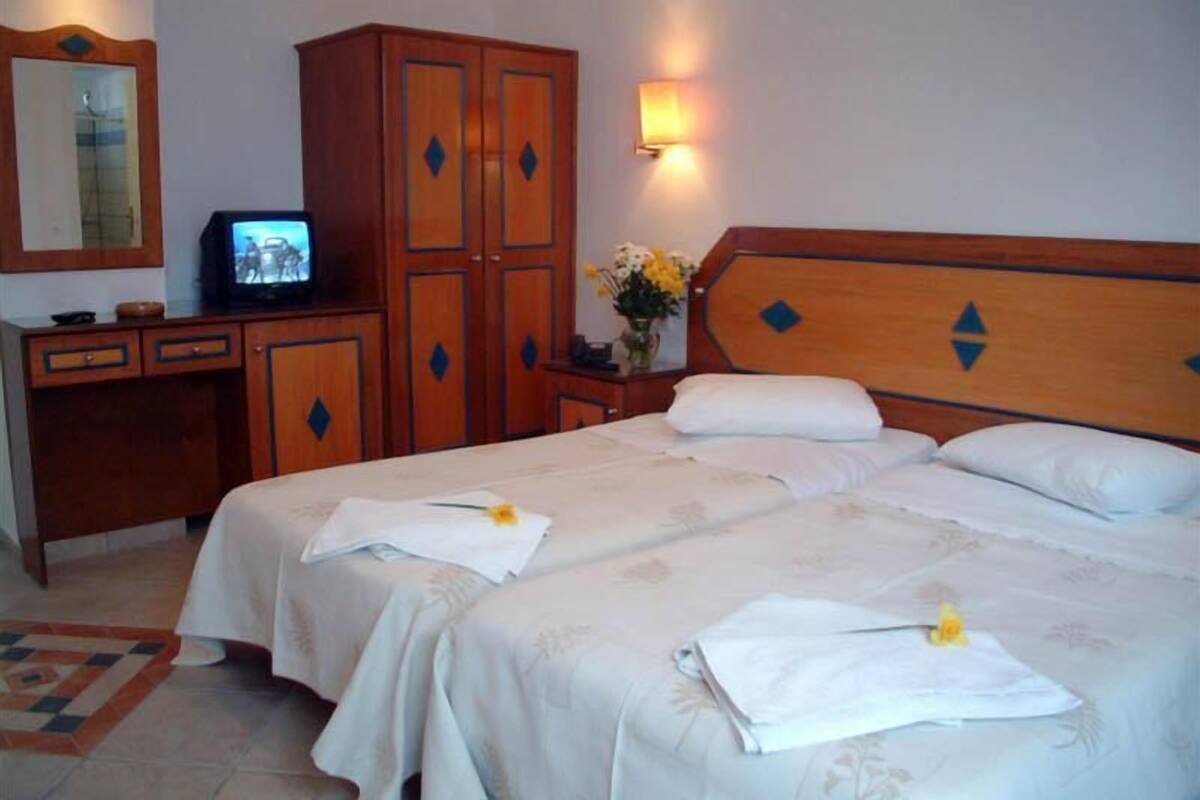 A hotel room with two beds, wooden wardrobe, a television, and a vase with flowers.