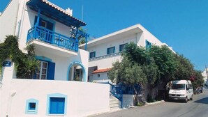 A white building with blue accents, including balconies and shutters, and a white van parked on the street. - Barbouni Hotel & Studios (Naxos)