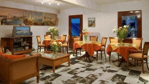 A dining area with tables set for four, surrounded by chairs, and a television on a stand. - Barbouni Hotel & Studios (Naxos)