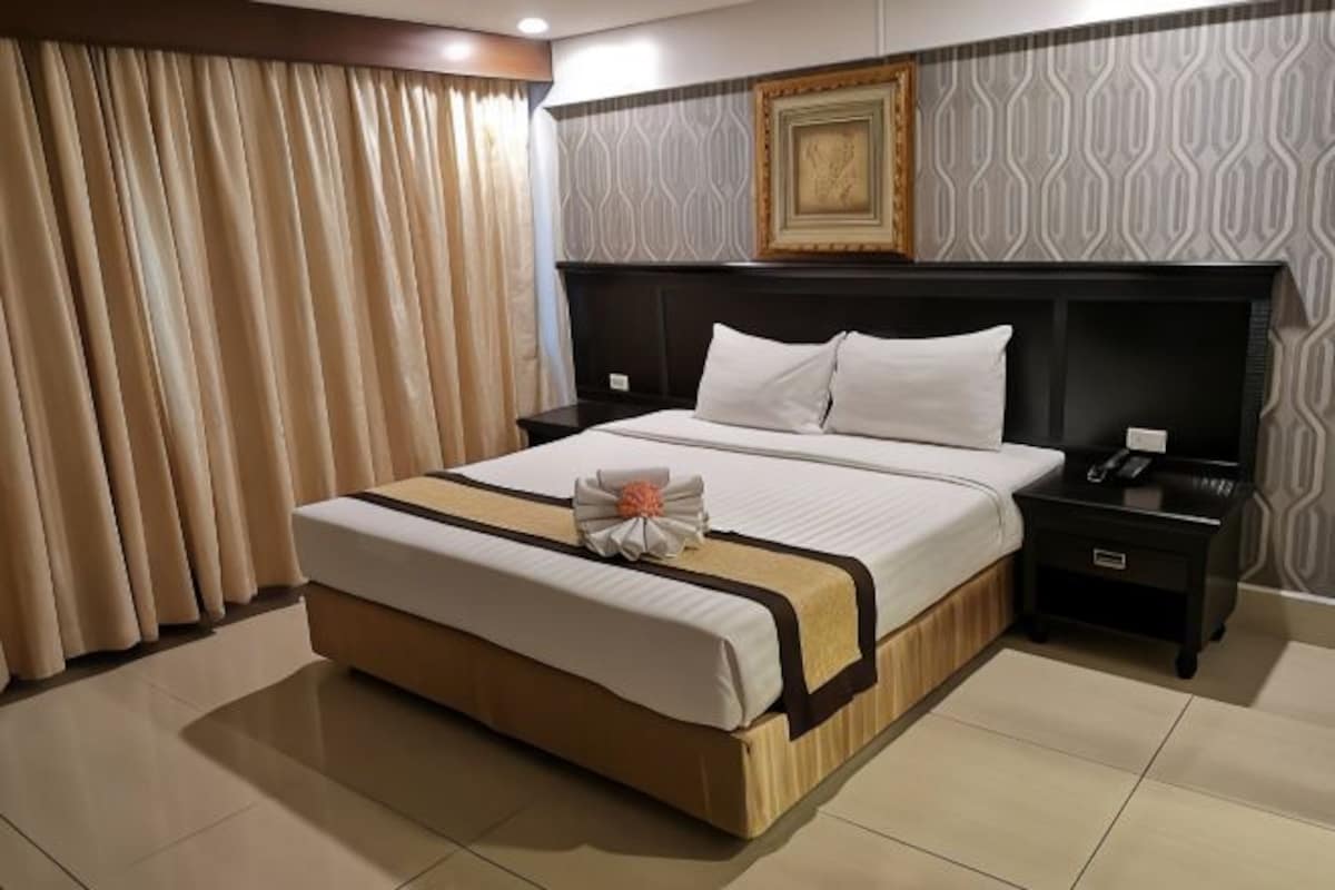 A hotel room with a large bed, a nightstand, a telephone, and a framed picture on the wall.