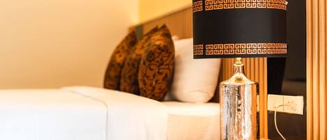 A bed with white bedding, a decorative lamp with a patterned shade, and a wooden nightstand.