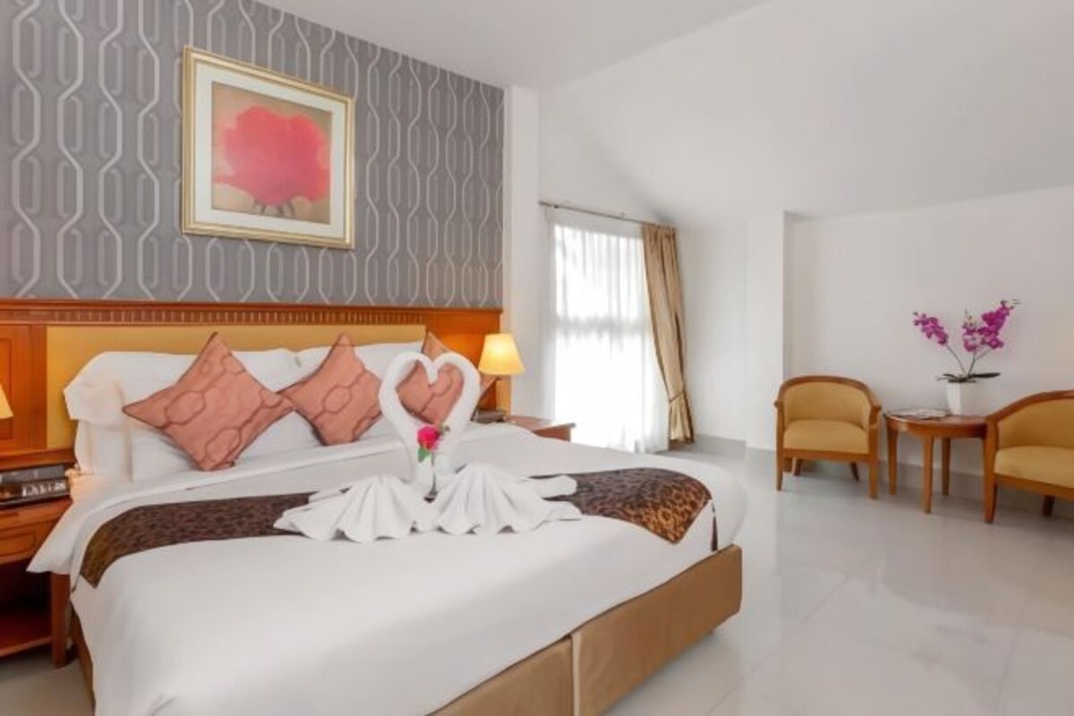 Un cuarto de hotel con una cama bien hecha, un cabecero con diseño estampado, un cuadro en la pared y una mesita de noche con una lámpara.