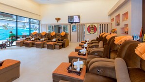 A spa area with multiple massage chairs, a television, and a large window with a view of a pool. - The Golden Ville Boutique Hotel & Spa (Pattaya)