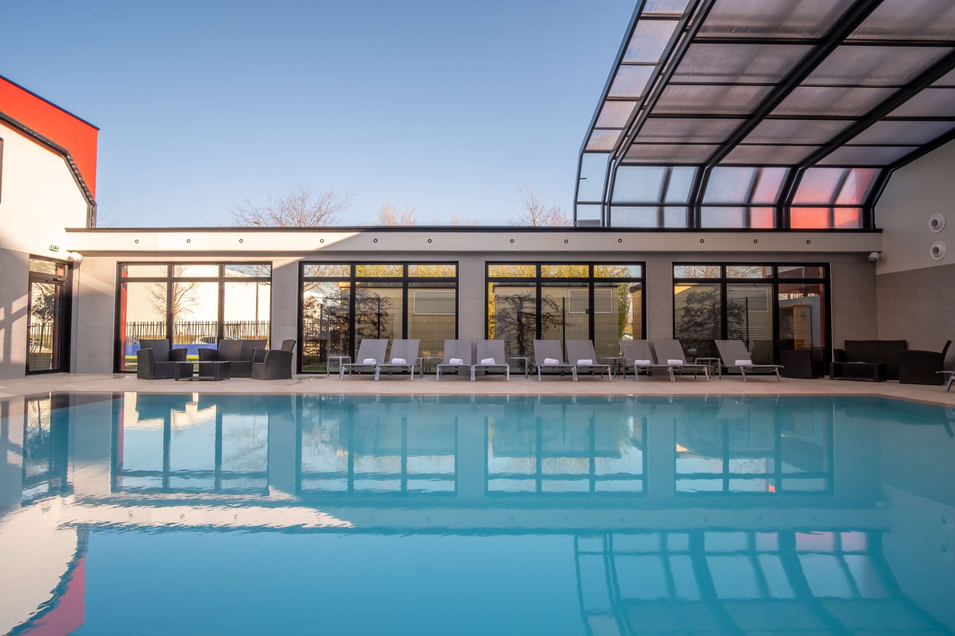 A modern pool area with clear glass walls, sun loungers, and a large pool.