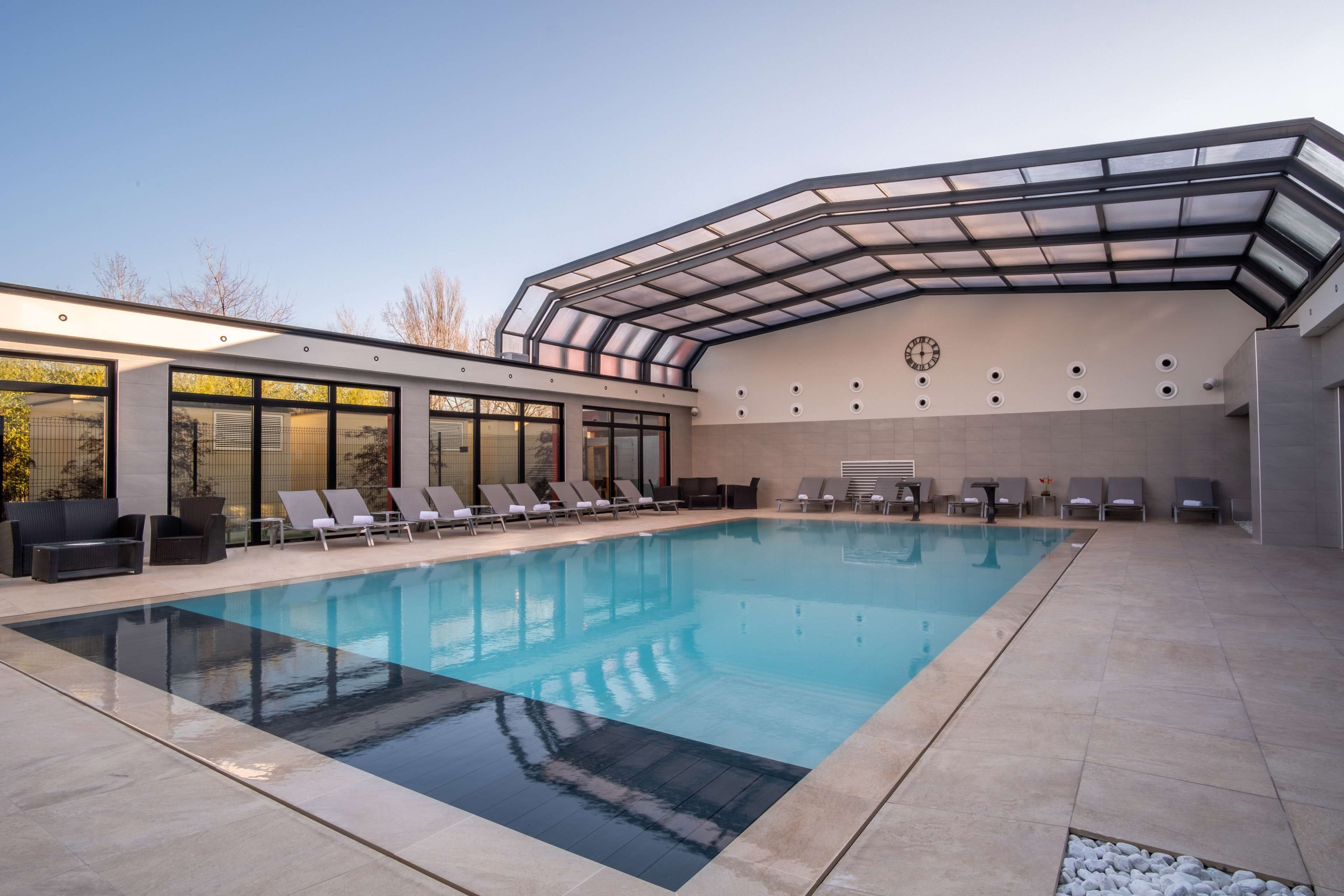 A modern indoor swimming pool with lounge chairs and a covered area.