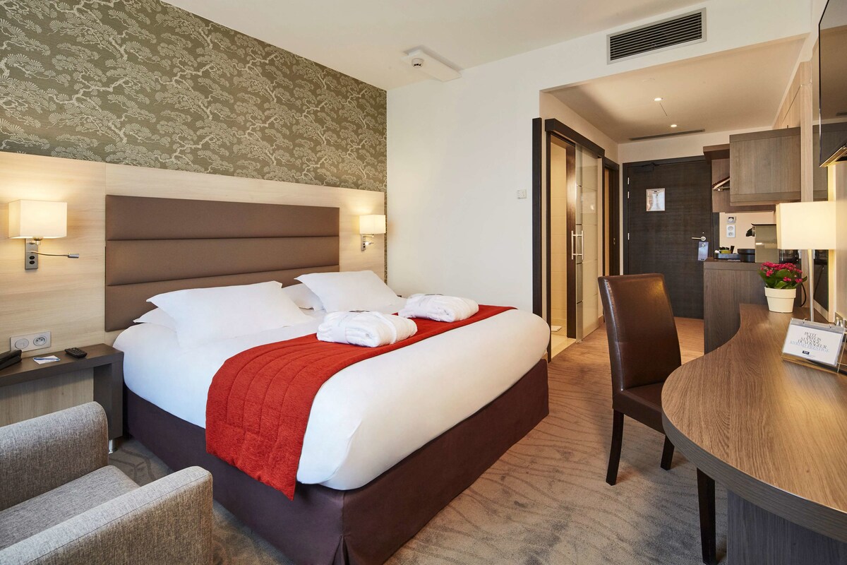 Habitación de hotel con una cama grande, un escritorio y una silla. Se ve un baño por una puerta abierta.
