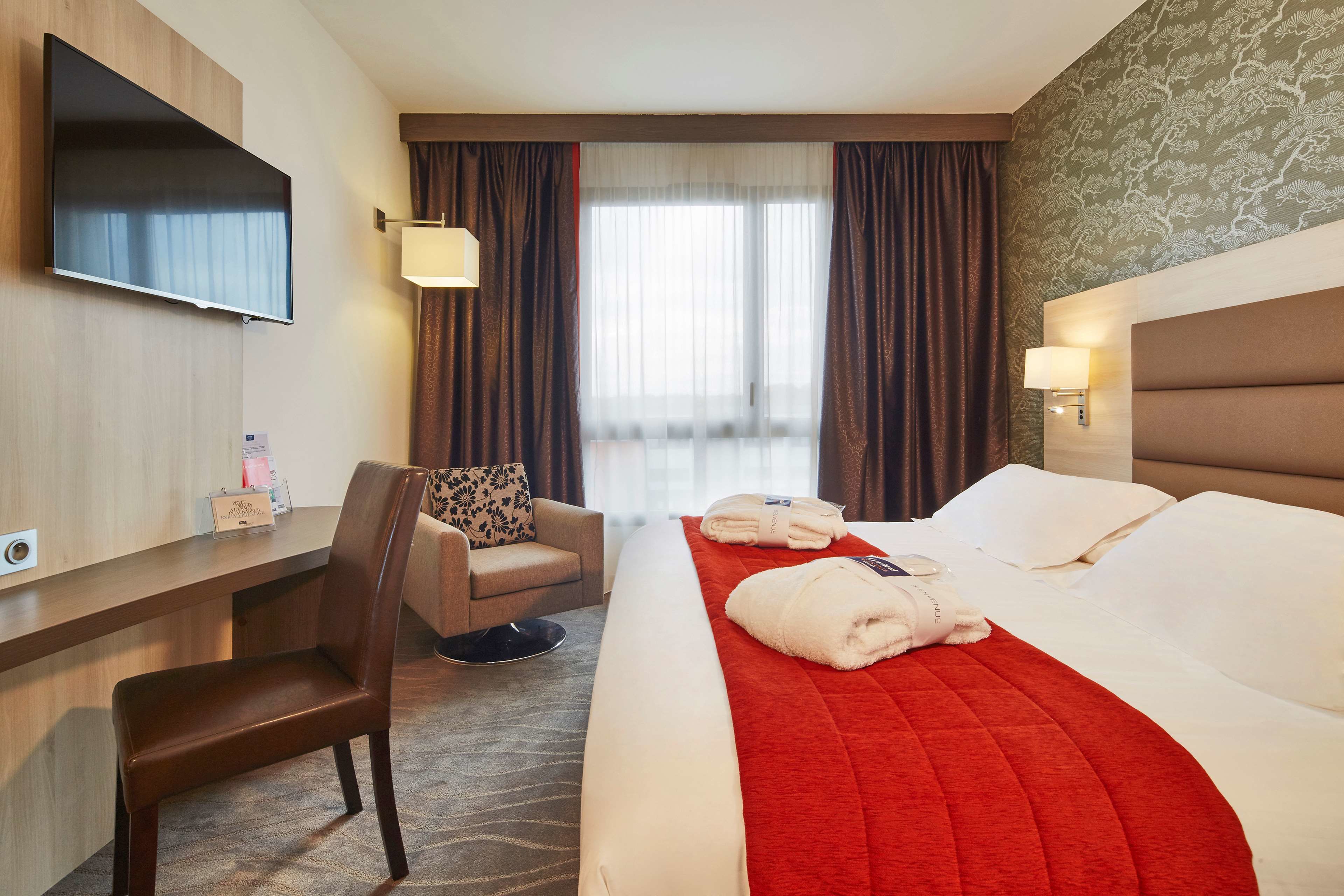 A hotel room with a bed, a desk, a chair, a TV, and a window with curtains.