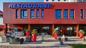 Un restaurante moderno con fachada roja, mesas al aire libre y plantas en macetas.