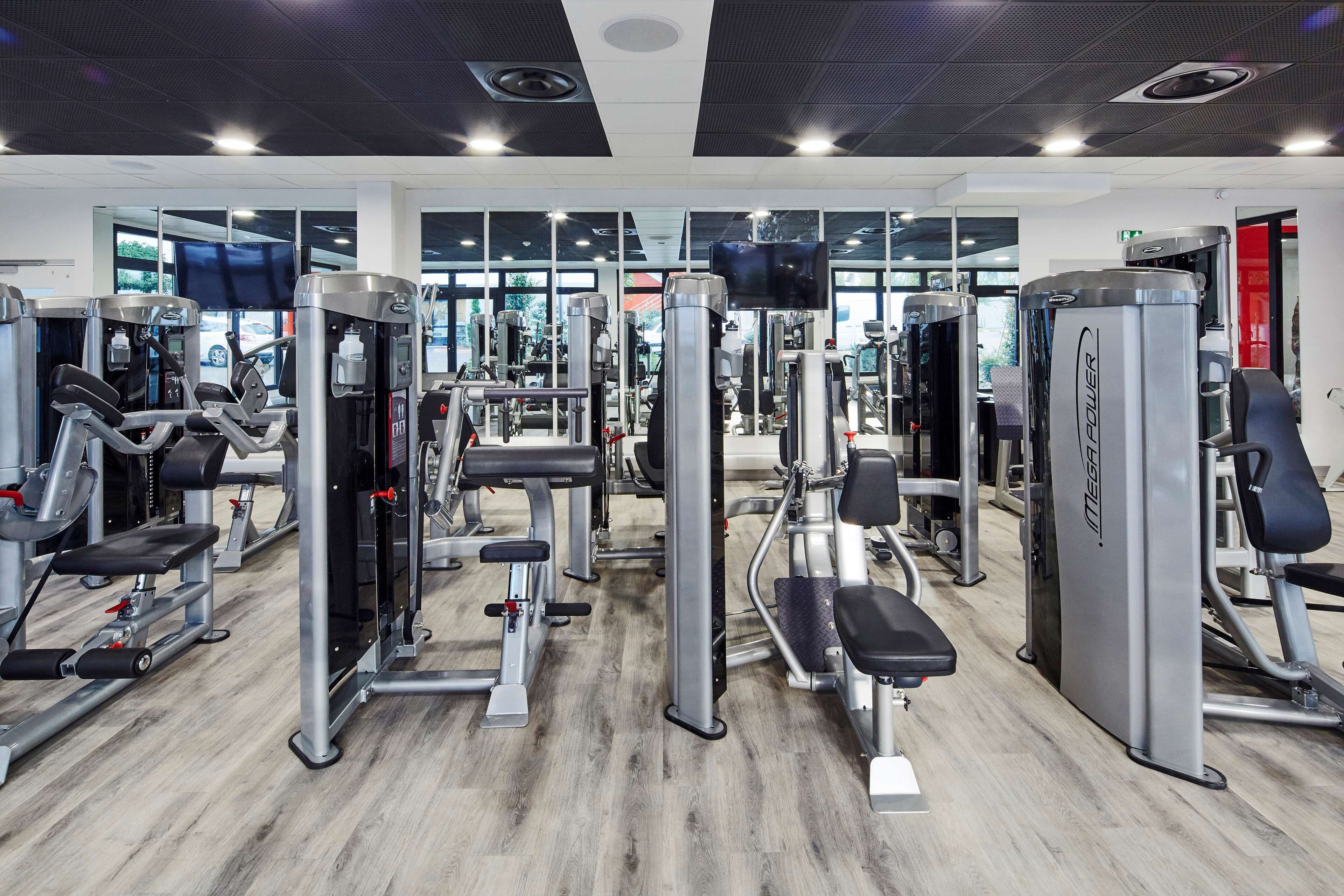A gym with various exercise machines, large windows, and a modern design.