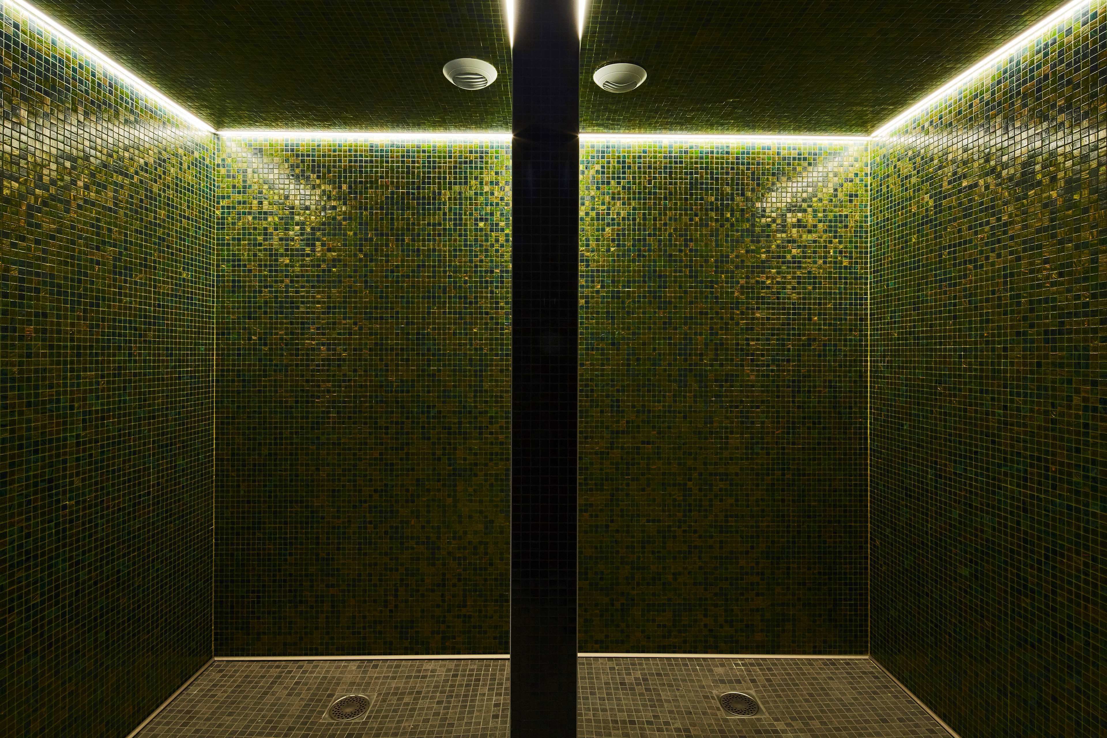 A tiled shower with a central column, recessed lighting, and a drain in the floor.