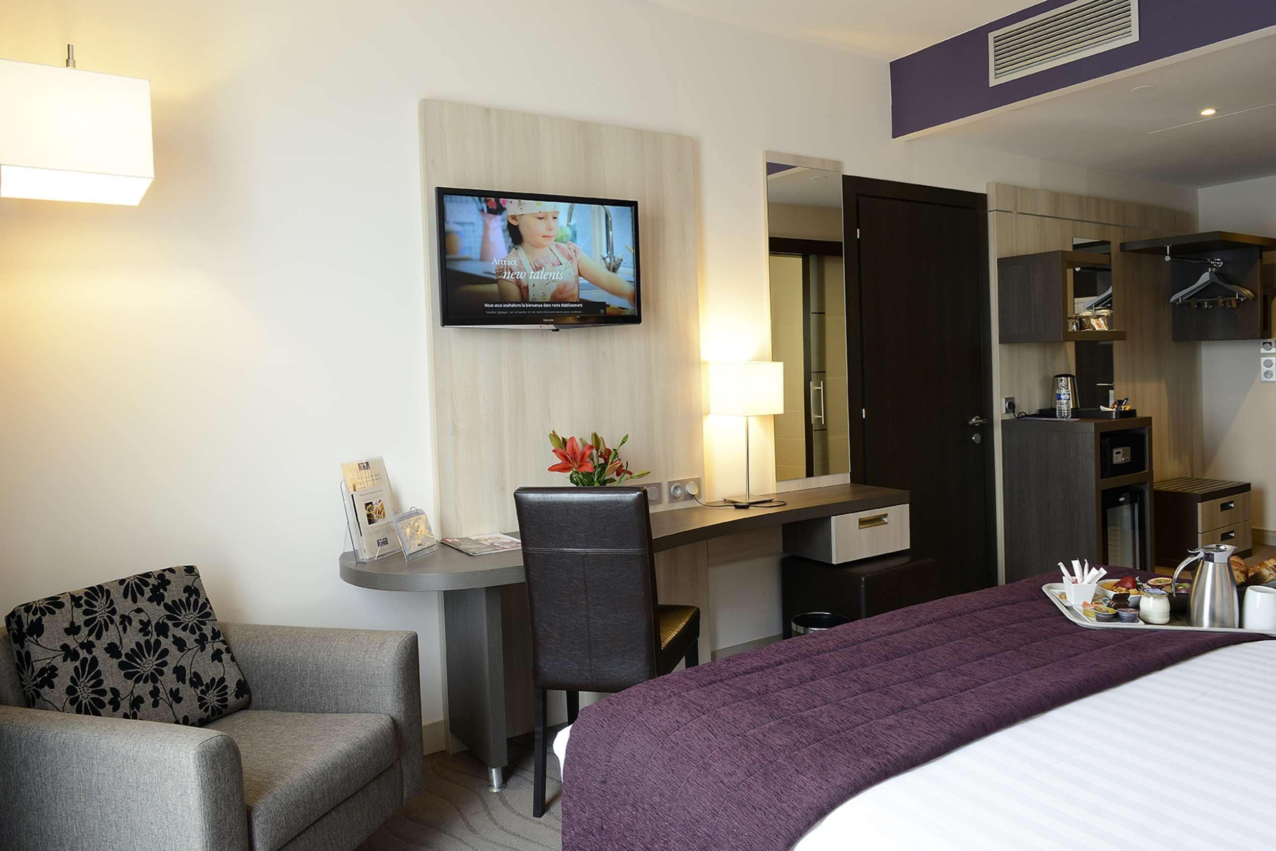 Habitación de hotel con cama, escritorio, silla, televisor y kitchenette.