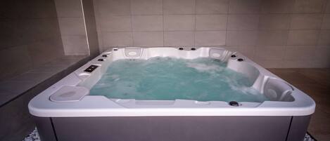 Una bañera de hidromasaje rectangular con múltiples chorros, rodeada de guijarros blancos, en un cuarto con baldosas.